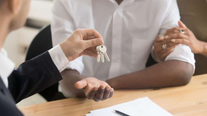 A man hands a couple a key to their new home