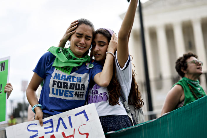 Protesters in front the Supreme Court building embrace with pained expressions and carry signs and wear shirts, one reading: March for our lives