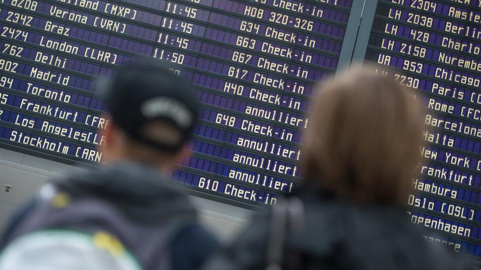 Reisende stehen vor einer Abflugtafel im Flughafen in München. Die Steuern auf Flugtickets sollen zum April 2020 steigen.