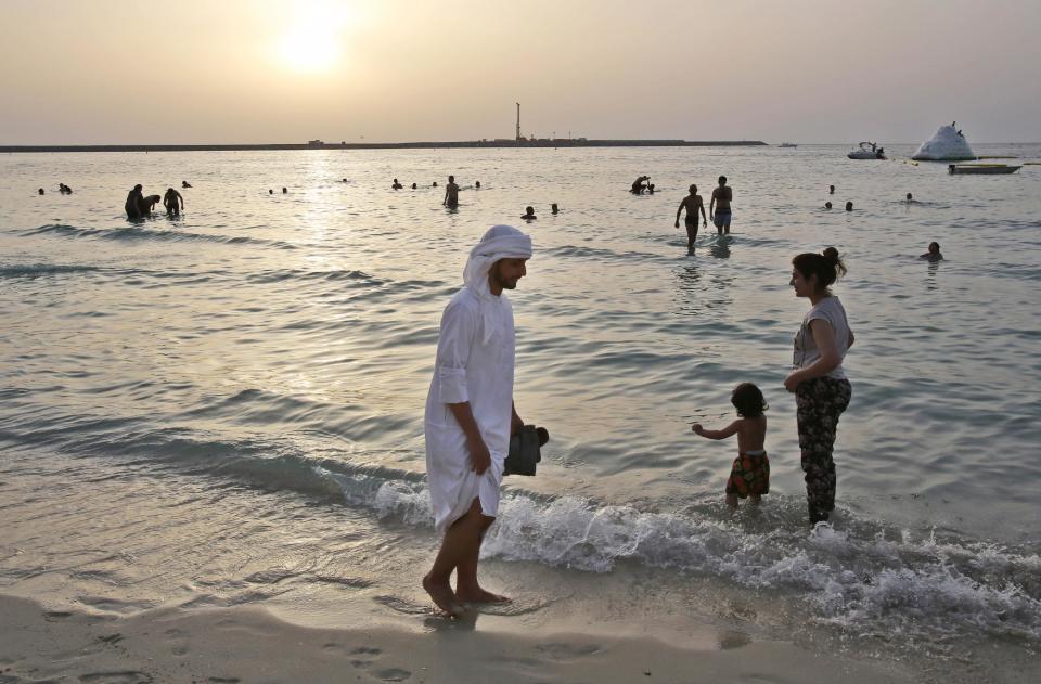 In this Saturday, April 19, 2014 photo, an Emirati man walks on the beach as the sun sets in Dubai, United Arab Emirates. The ribbon of beach nestled along the towering skyscrapers rising from Dubai’s man-made marina district is a rare spot in the Middle East, bringing together the conservatively dressed and the bikini-clad in a multiethnic mix of those with means and those still striving for a more comfortable life. (AP Photo/Kamran Jebreili)