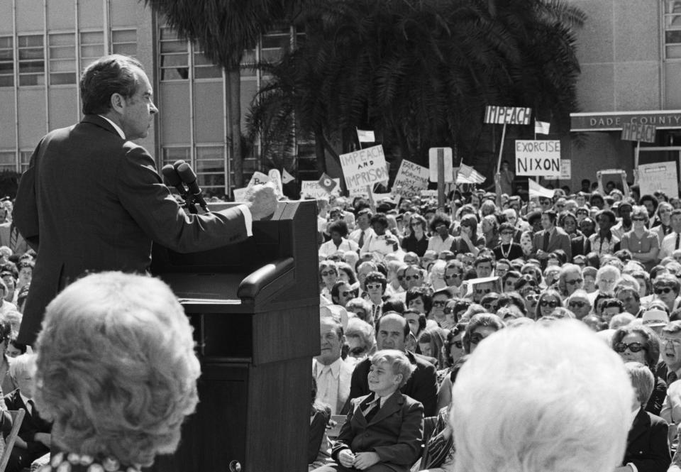 Pres. Richard M. Nixon addresses a gathering at dedication ceremonies of the Cedars of Lebanon Health Care Center. In the background are protesters carrying signs asking for his impeachment and 