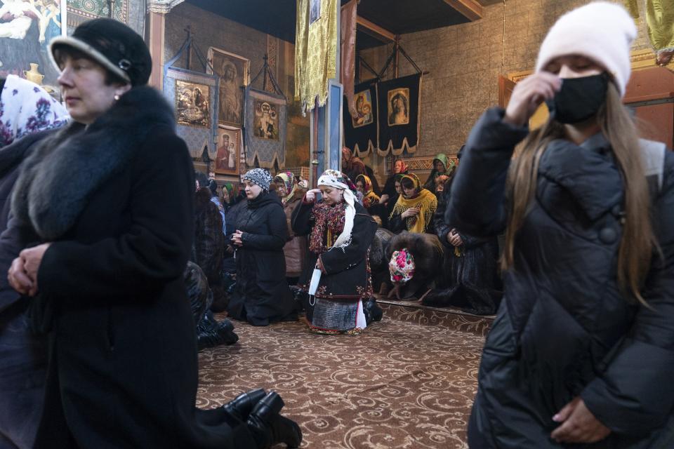 Dr. Viktoria Mahnych, wearing a Hutsul's traditional colorful clothes, center, crosses herself holding a face mask in her hand because other worshippers forced her to take off her mask " in order not to remind about the contagion" in the Holy Trinity church during the Orthodox Christmas celebration in Iltsi village, Ivano-Frankivsk region of Western Ukraine, Thursday, Jan. 7, 2021. Mahnych fears that a lockdown in Ukraine came too late and the long holidays, during which Ukrainians frequented entertainment venues, attended festive parties and crowded church services, will trigger a surge in new coronavirus infections. (AP Photo/Evgeniy Maloletka)