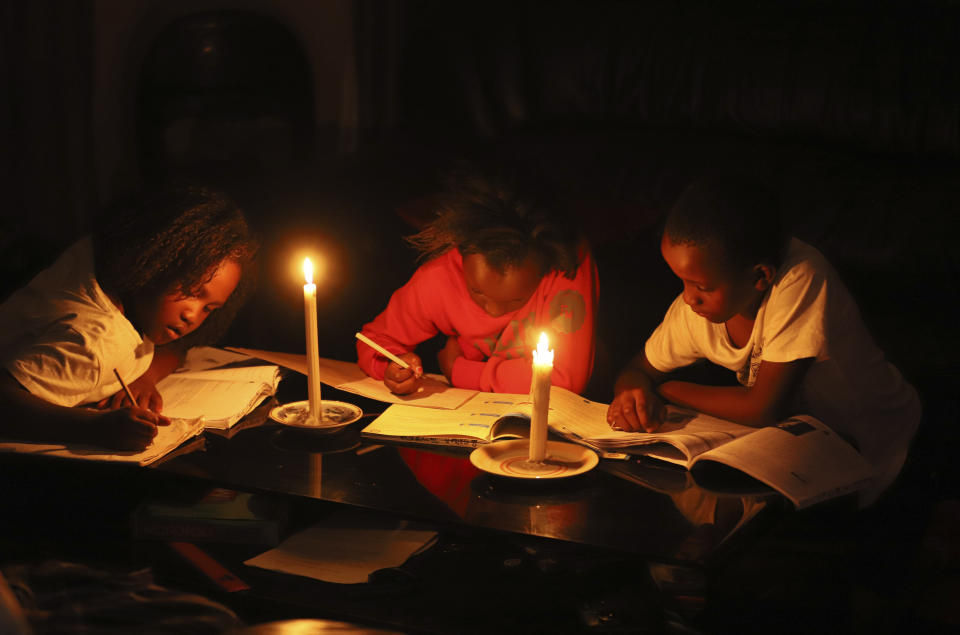 Children study by candle light at their home in Harare, Zimbabwe, Tuesday, Dec. 20, 2022. A buoyant holiday mood is not lifting the country which is coping with widespread power outages and the world's highest food inflation. (AP Photo)