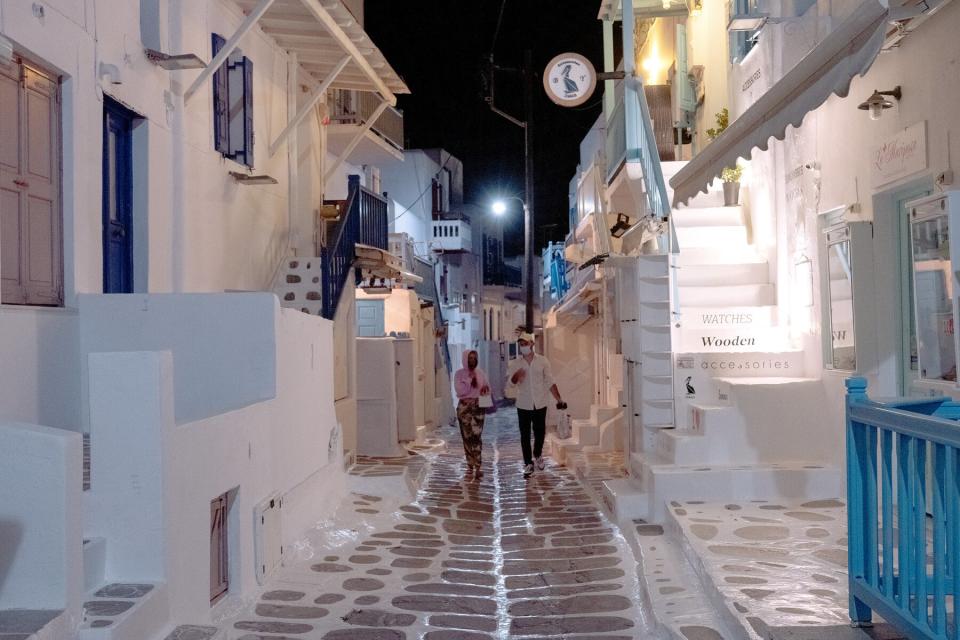 Pedestrians walk along an empty street in the evening ahead of the return of tourists in Mykonos, Greece, on Sunday, May 9, 2021.