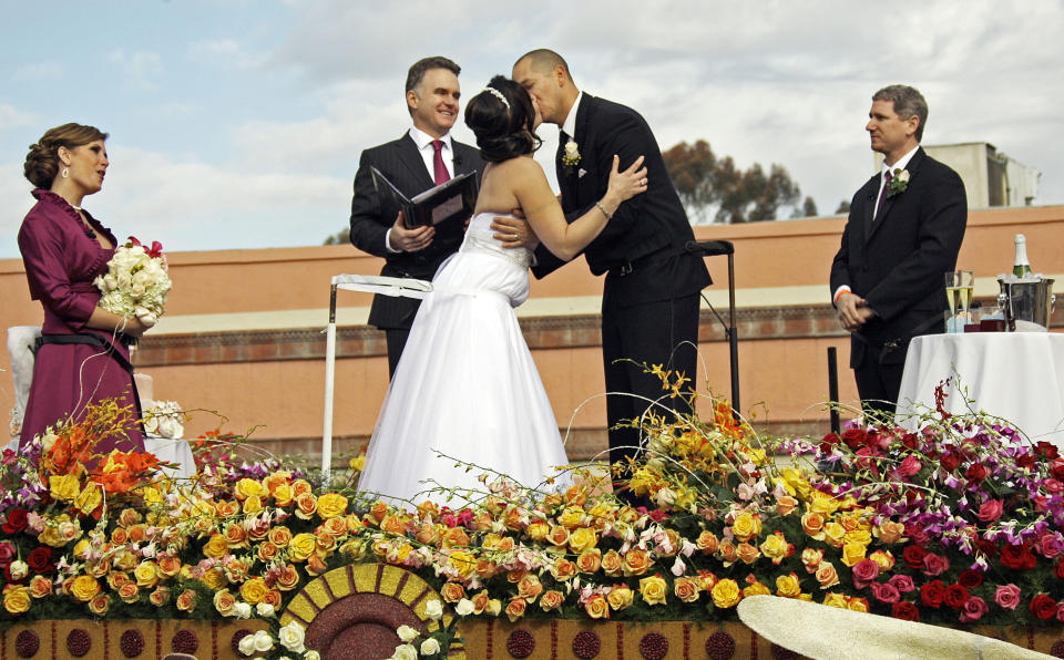 Newlyweds Nicole Angelillo and Gerald Sapienza, both of Chesapeake, Va., kiss aboard the Farmers Insurance The Love Float, in the 124th Rose Parade in Pasadena, Calif., Tuesday, Jan. 1, 2013. The couple, married aboard the float just minutes earlier by nationally syndicated radio personality Sean Valentine, center, are the winners of a national promotion by Farmers. Others are unidentified. (AP Photo/Reed Saxon)