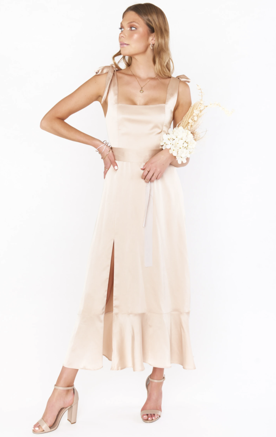 blone model posing with hand on hip in nude silk bridesmaids dress holding bouquet of flowers