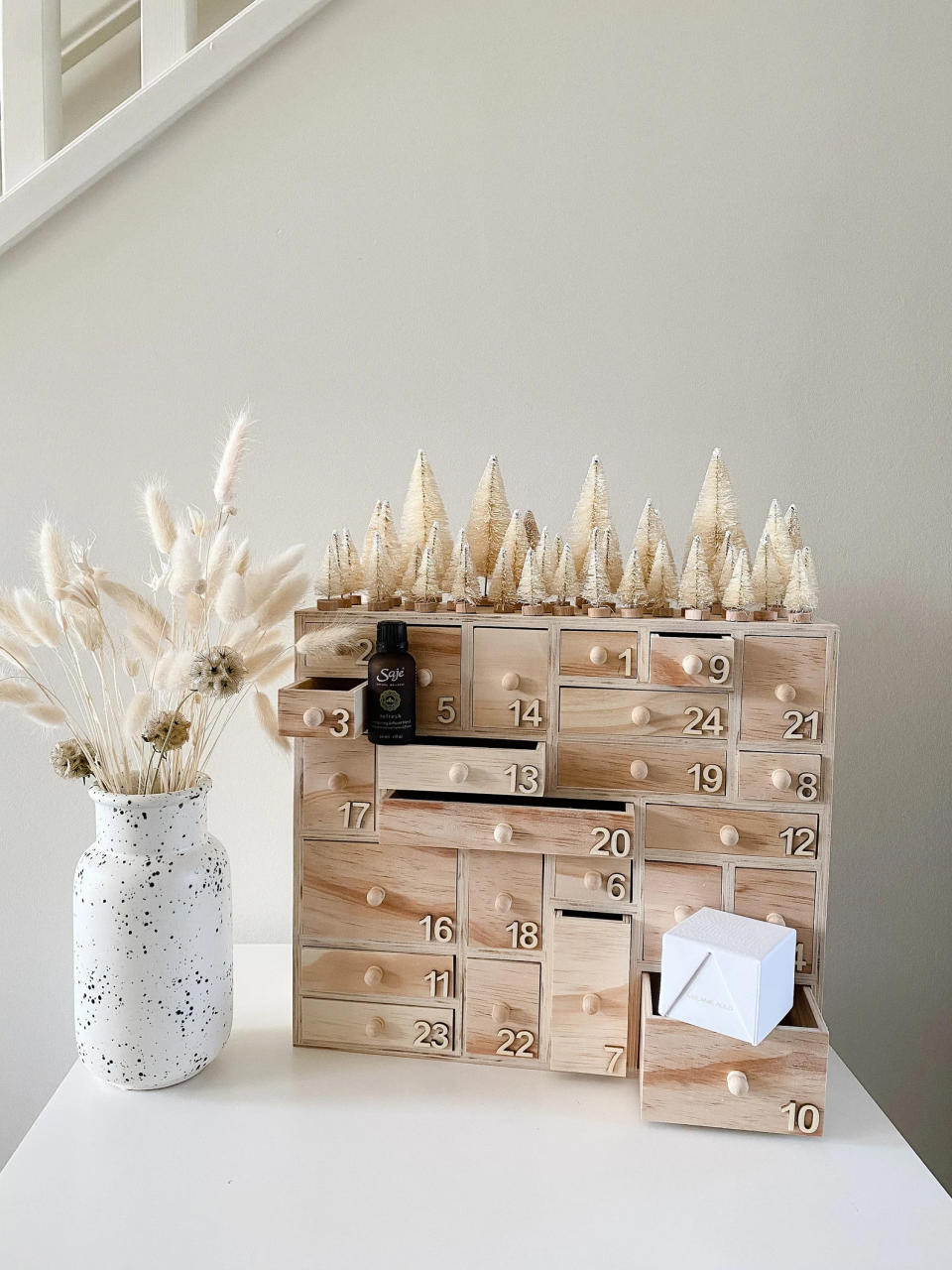 the Handcrafted Wooden Advent Calendar on a surface beside a vase with dried plants
