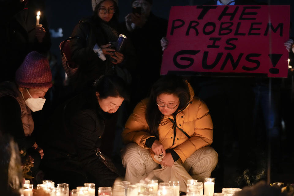 Women place candles at a memorial while a man holds a sign during a vigil outside Monterey Park City Hall, blocks from the Star Ballroom Dance Studio on Tuesday, Jan. 24, 2023, in Monterey Park, Calif. A gunman killed multiple people at the ballroom dance studio late Saturday amid Lunar New Years celebrations in the predominantly Asian American community. (AP Photo/Ashley Landis)