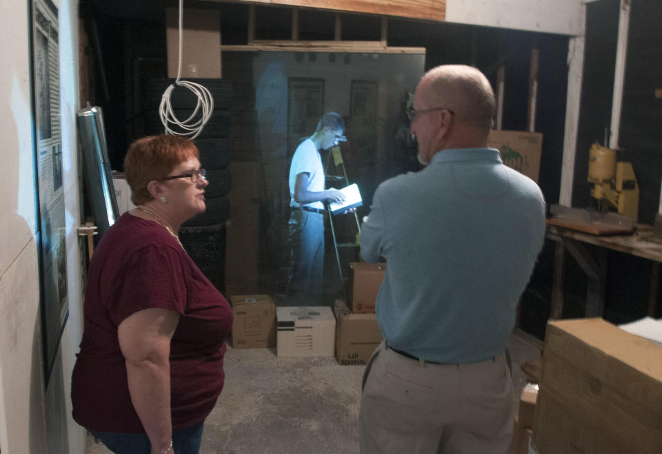 CORRECTS DATE OF MUSEUM OPENING TO NOV. 6 - In this Oct. 29, 2013 photo, Shirley Smith, capital improvement program coordinator for the city of Irving, Texas, left, and building inspector Lawrence Crow talk in the garage at the Ruth Paine House Museum, in Irving. The museum in the small, two-bedroom home that once belonged to Ruth Paine, who had befriended Lee Harvey Oswald’s wife Marina and let her live there with her two daughters, will open Wednesday, Nov. 6, 2013. In the background is a projection of an actor portraying Lee Harvey Oswald using a technique called Pepper's Ghost. (AP Photo/Rex C. Curry)
