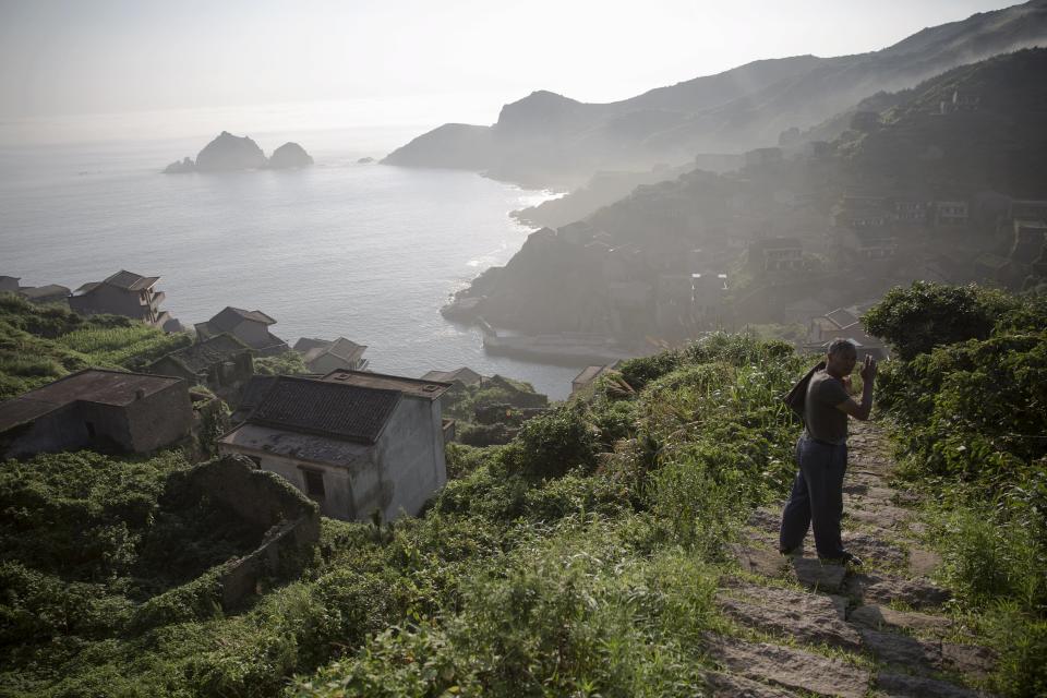 A former resident who is engaged by the local government to assist visiting tourists arrives in the abandoned fishing village of Houtouwan on the island of Shengshan as mist rises early July 26, 2015. (REUTERS/Damir Sagolj)
