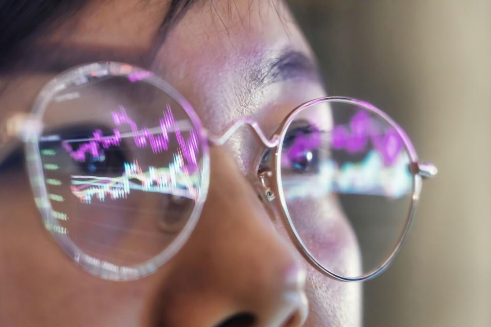 A person wearing eyeglasses with the reflection of stock charts showing on the glasses.