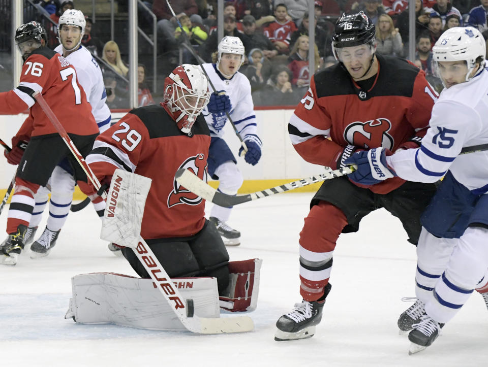 New Jersey Devils goaltender Mackenzie Blackwood (29) deflects the puck as Devils center Kevin Rooney (16) and Toronto Maple Leafs center Alexander Kerfoot (15) chase after the puck during the first period of an NHL hockey game Friday, Dec. 27, 2019, in Newark, N.J. (AP Photo/Bill Kostroun)