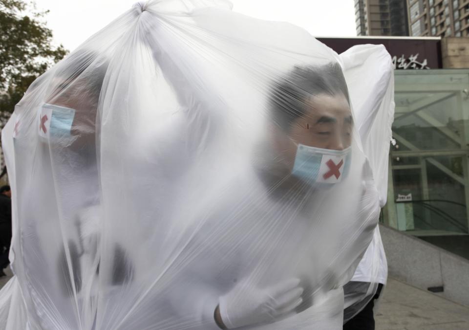 College students wearing masks cover themselves with plastic bags as they participate in a performance art to raise awareness of air pollution, in Xi'an