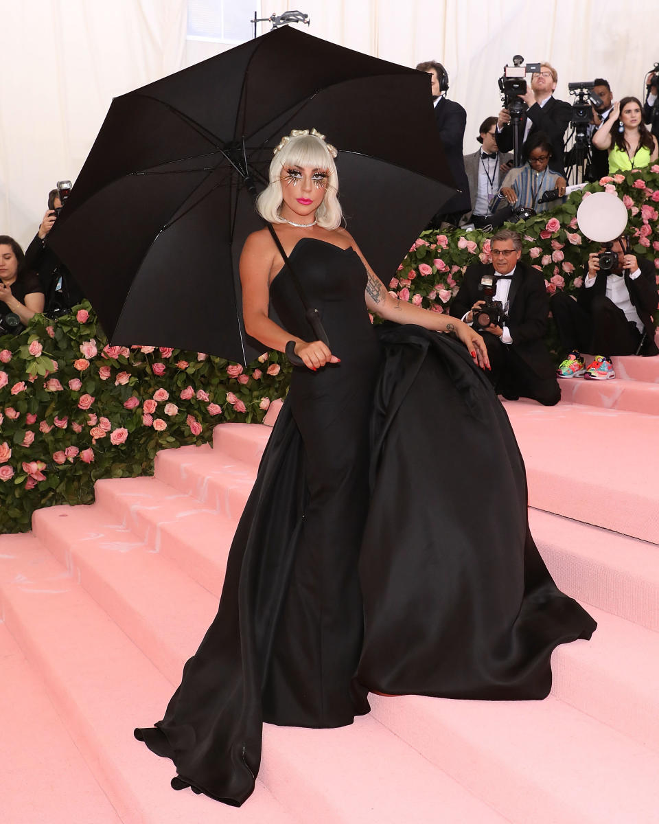 Lady Gaga at an event wearing an elegant dark gown with a large black umbrella