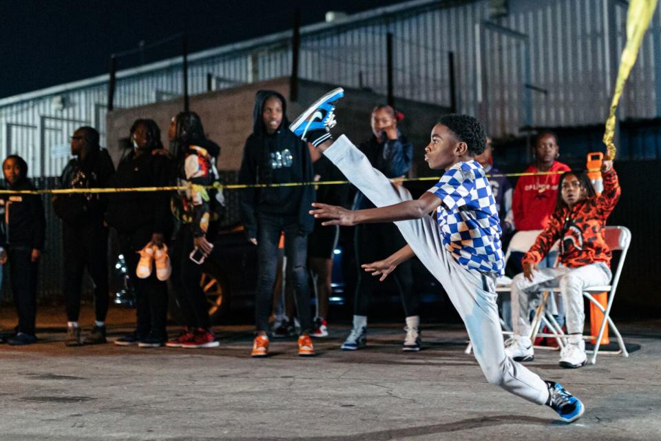 A kid kicks his leg up during a dance battle.