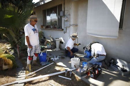 Manuel Rodriguez, 83, (L) watches as workmen install a water pump to carry water from an outdoor container into his home in Porterville, California October 14, 2014.REUTERS/Lucy Nicholson