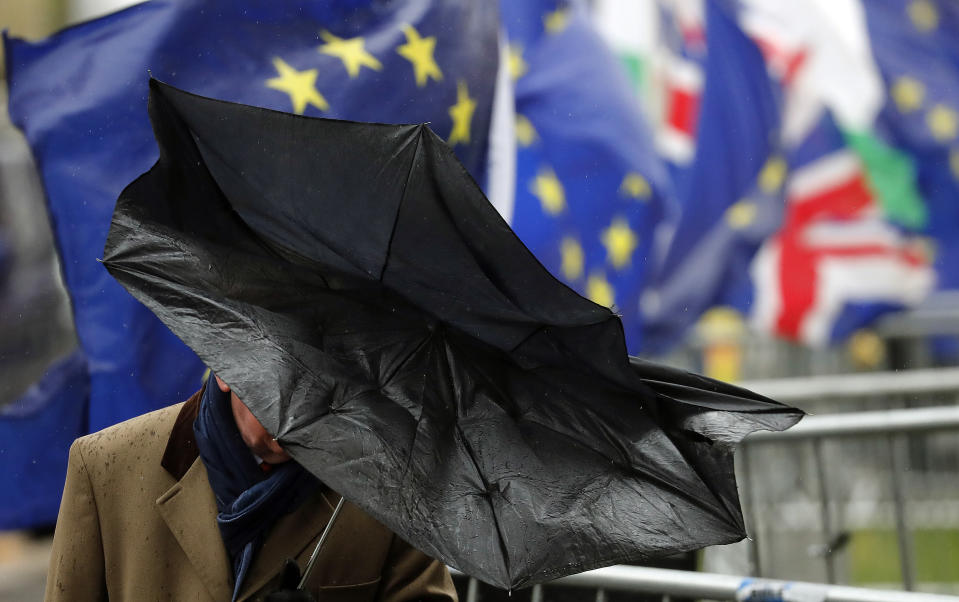 A man shelters with an umbrella as he walks by Pro EU protestors holding flags opposite the Houses of Parliament in London, Thursday, April 4, 2019. The British government and senior opposition figures were meeting Thursday in search of a new plan on how the country leaves the European Union as Prime Minister Theresa May tried to stop her shift toward compromise from splitting her Conservative Party. (AP Photo/Frank Augstein)