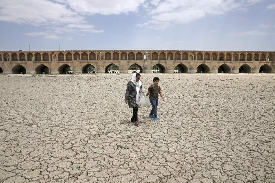 FILE - In this Tuesday, July 10, 2018 file photo, a woman and a boy walk on the dried up riverbed of the Zayandeh Roud river that no longer runs under the 400-year-old Si-o-seh Pol bridge in Isfahan, Iran. With global temperatures rising, superstorms taking their deadly toll and a year-end deadline to firm up the Paris climate deal, leaders at this year’s U.N. General Assembly are feeling a sense of urgency to keep up the momentum on combating climate change. (AP Photo/Vahid Salemi, file)