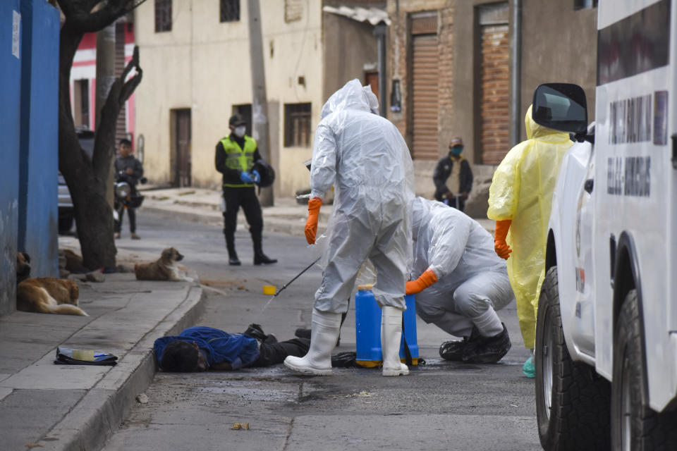 Trabajadores de salud con equipo para protegerse del coronavirus desinfectan el cadáver de un vendedor ambulante el sábado 25 de julio de 2020 en el vecindario Cerro San Miguel, en Cochabamba, Bolivia. (AP Foto/Dico Solís)