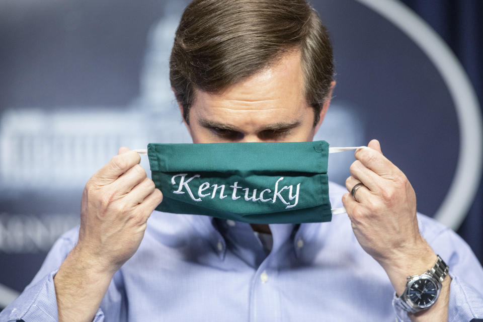 FILE - In this May 11, 2020, file photo, Kentucky Gov. Andy Beshear puts on a face mask after speaking to reporters at the Capitol in Frankfort, Ky. Kentucky's governor said Sunday, Oct. 11, 2020, that he will quarantine after a member of his security detail who drove with his family the day before later tested positive for COVID-19. Democratic Gov. Andy Beshear said he and his family feel fine, show no coronavirus symptoms and have tested negative for the virus. (Ryan C. Hermens/Lexington Herald-Leader via AP, File)