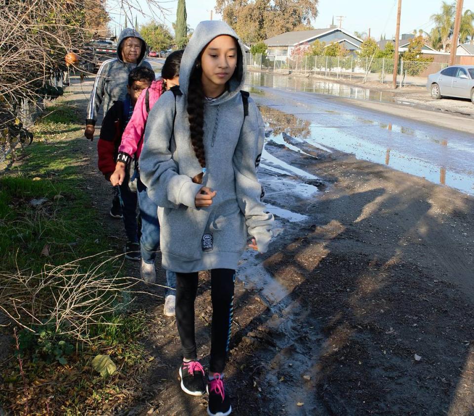 Maria Murillo (rear) escorts grandchildren Yazmannie (front), Jaylannie and Armando along a muddy Dallas Street in south Modesto CA on Dec. 6, 2022. Nearby streets will get sidewalks thanks to a $2.38 million state grant, but much of the area will continue to lack them.