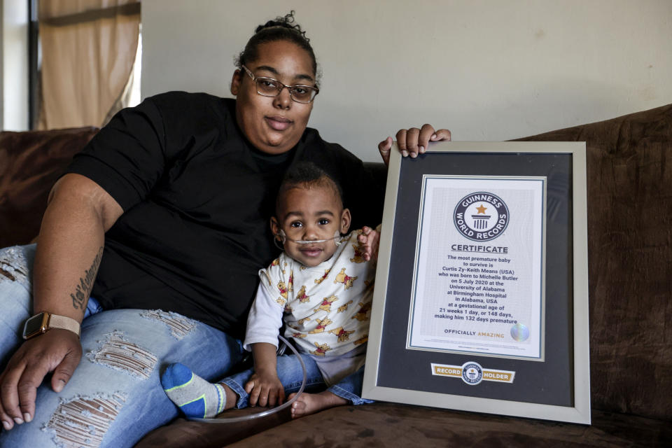 Curtis Means and his mother, Michelle Butler, sit with their certificate from the Guinness Book of World Records at their home in Eutaw, Ala., on Wednesday, March 23, 2022. In July 2020, Curtis became the earliest surviving “micropreemie” in the world. (AP Photo/Butch Dill)