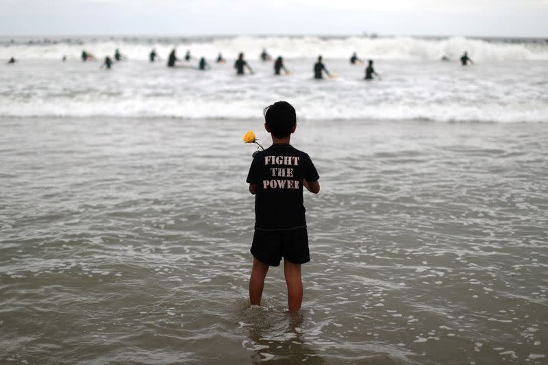 A boy holds a rose as he watches surfers at The Black Girls Surf paddle-out in memory of George Floyd,who died in Minneapolis police custody, in Santa Monica