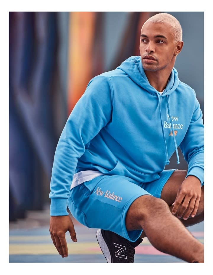 A man sits perched on one toe stretching in sky blue hoodie with matching shorts 