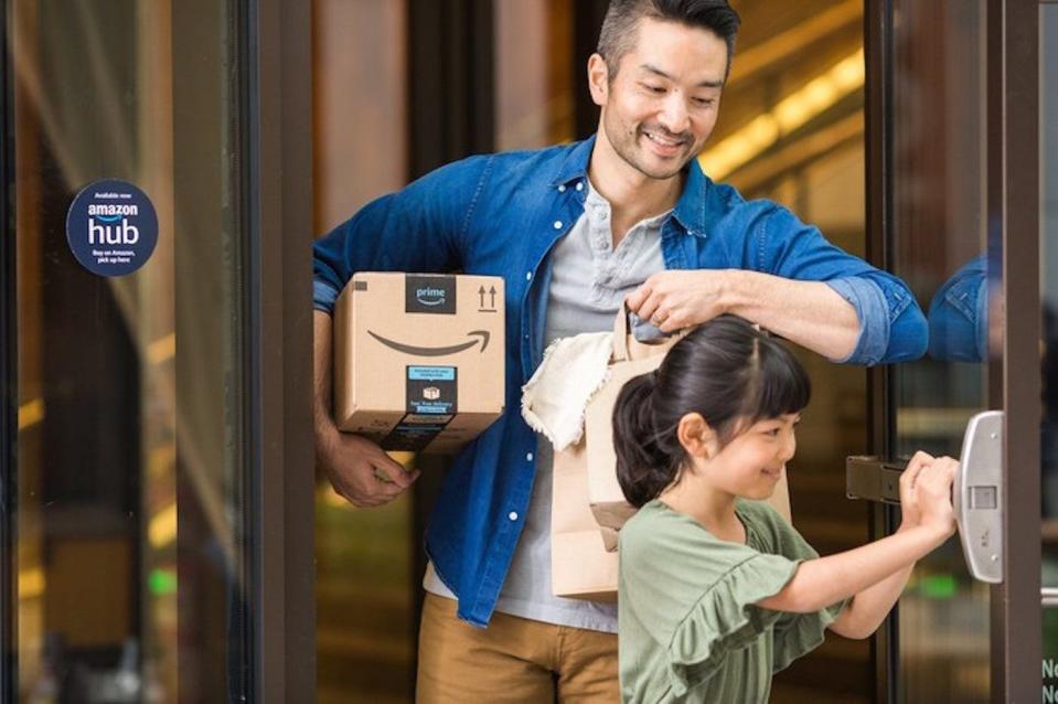 A parent holding an Amazon package under their right arm, while their child holds a door open for them.