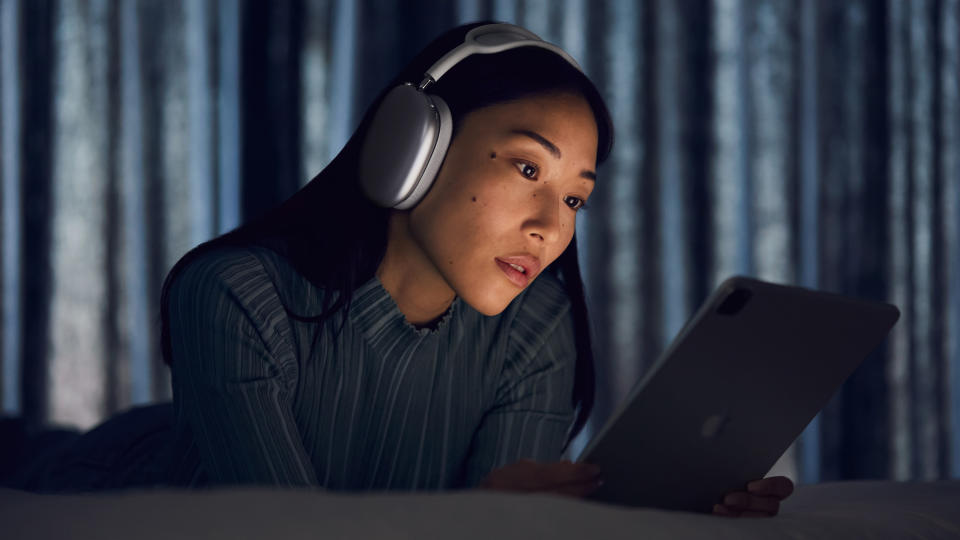 Woman wearing Apple Airpods Max while looking at Apple iPad in a dark room