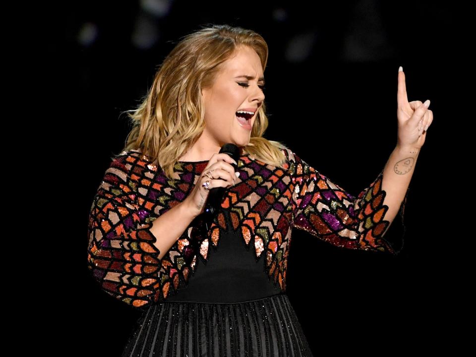 Adele singing with her eyes shut and pointing on finger into the air.