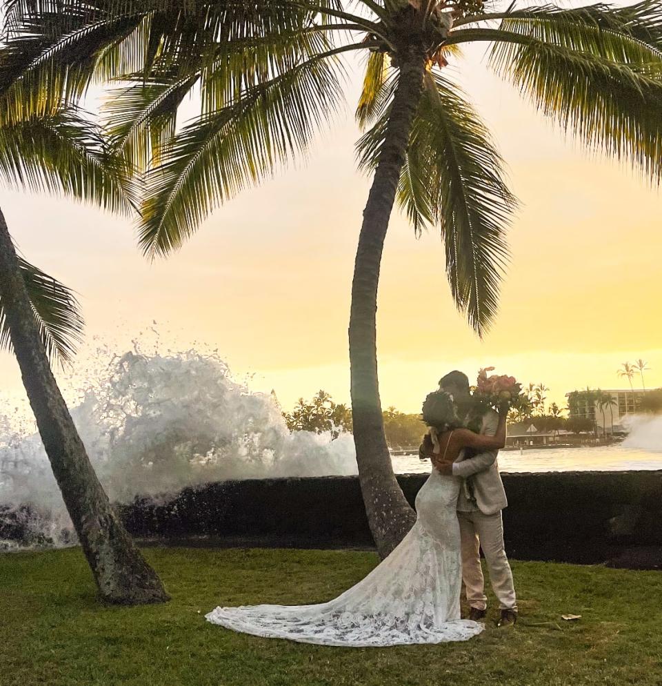 A bride and groom kiss in front of a sunset and giant wave crashing over a sea wall (Courtesy of Dillion and Riley Murphy)