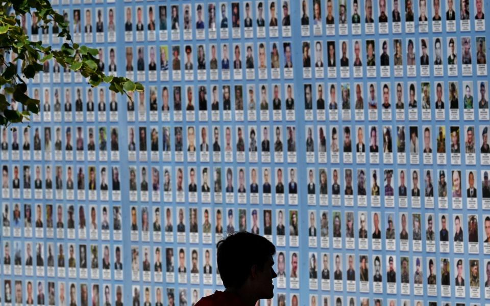 A man sits and looks at a memorial wall displaying images of Ukrainian troops killed since Russia invaded Ukraine - SERGEI SUPINSKY/AFP