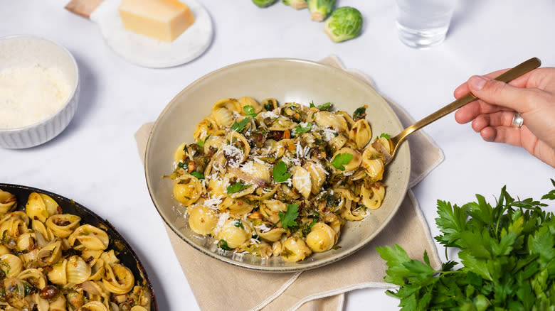 hand taking fork of orecchiette pasta with parmesan and parsley in bowl