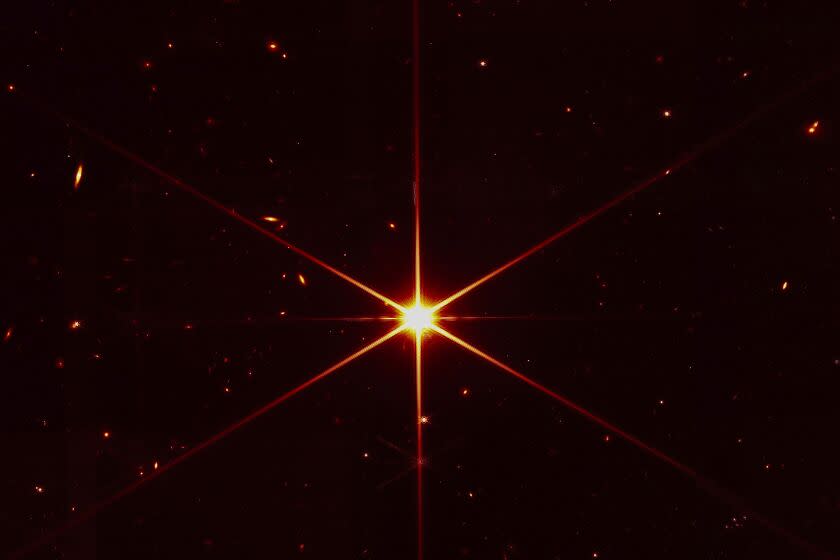 This image made available by NASA on Wednesday, March 16, 2022 shows star 2MASS J17554042+6551277 used to align the mirrors of the James Webb Space Telescope, with galaxies and stars surrounding it. The hexagonal shape of Webb's mirrors and its filters made the shimmering star look more red and spiky. The first science images aren't expected until late June or early July. (NASA/STScI via AP)