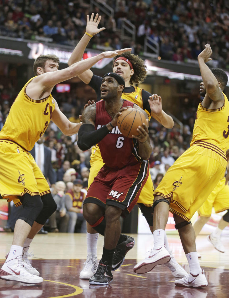 Miami Heat's LeBron James, center, drives between Cleveland Cavaliers' Spencer Hawes, left; Anderson Varejao, rear, from Brazil; and Alonzo Gee, right, during the third quarter of an NBA basketball game Tuesday, March 18, 2014, in Cleveland. Miami defeated Cleveland 100-96. (AP Photo/Tony Dejak)