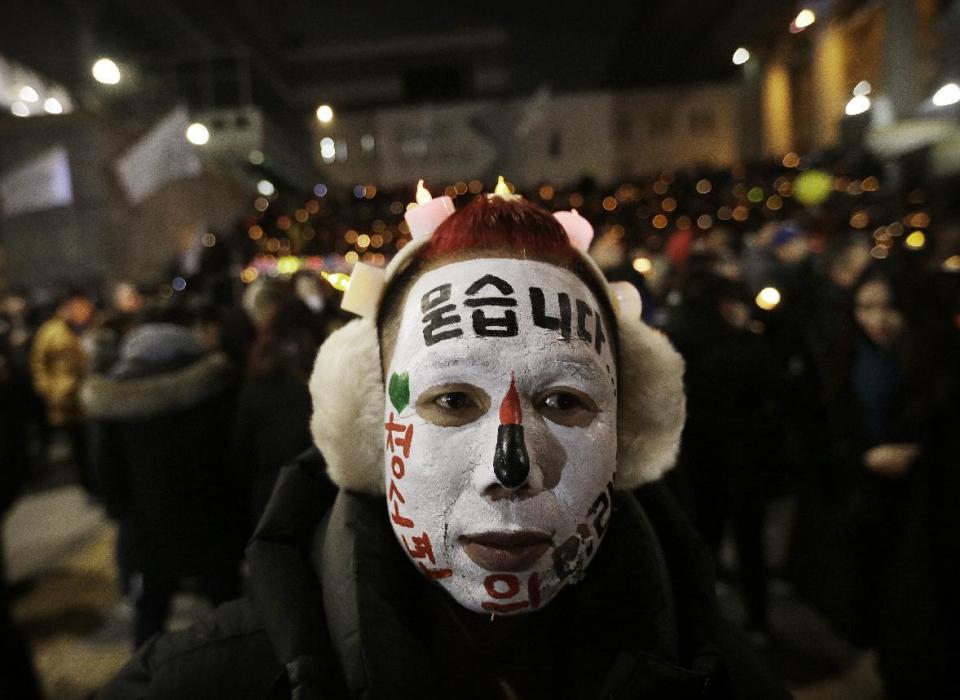 A protester with his face painted attends a candle light vigil calling for impeached President Park Geun-hye to step down in Seoul, South Korea, Saturday, Dec. 31, 2016. Even on New Year's Eve, large crowds of South Koreans gathered to join another rally demanding the ouster of impeached President Park Geun-hye, who's determined to restore her powers through a court trial. The letters read " Asking". (AP Photo/Ahn Young-joon)