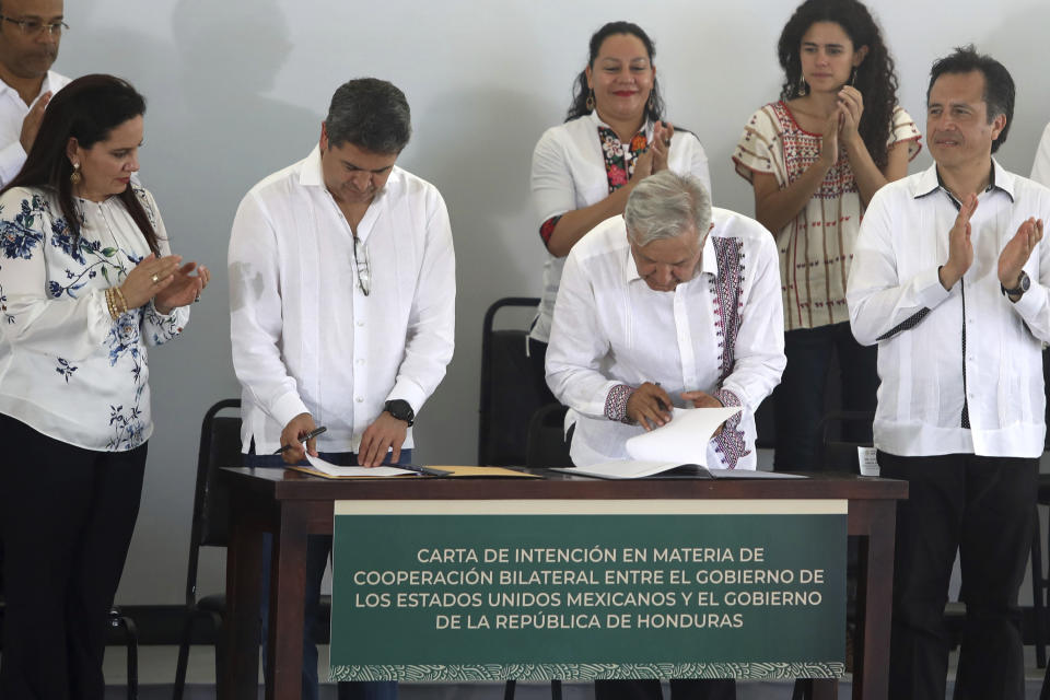 Honduras' President Juan Orlando Hernandez, center left, and Mexico's President Andrés Manuel López Obrador, sign an agreement as part of the Mexican program "Sembrando Vida," on a military base in Minatitlan, Mexico, Saturday, July 27, 2019. Lopez Obrador said Saturday that Honduras will adopt a Mexican program to put people to work planting trees and also will copy a Mexican program which pays a small monthly stipend to young people while they are studying, in an effort to stem the tide of Central American migrants seeking asylum in the U.S. (AP Photo/Felix Marquez)