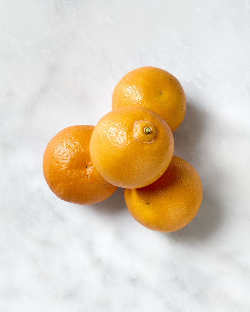 overhead shot of four clementines on a white marble surface.