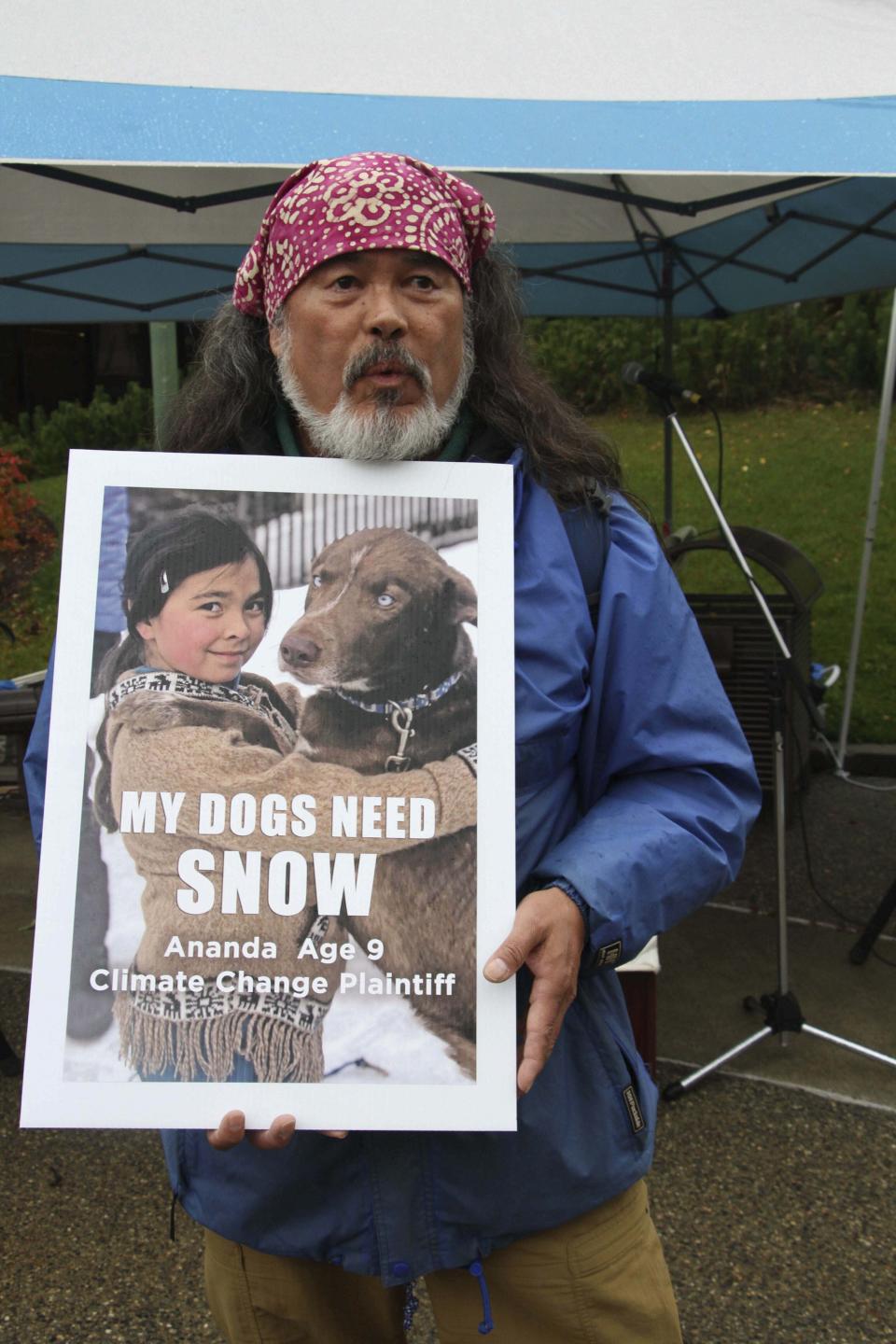 FILE - Dune Lankard of Cordova, Alaska, holds a sign showing his daughter, Ananda Rose, a budding musher, outside Boney Courthouse in Anchorage, Alaska, on Oct. 9, 2019. Ananda Rose is one of 16 Alaska youths who in 2017 sued the state, claiming that human-caused greenhouse gas emission leading to climate change is creating long-term, dangerous health effects. The Alaska Supreme Court on Friday, Jan. 28, 2022, upheld the dismissal of a lawsuit filed by the youths, who claimed long-term effects of climate change will devastate Alaska and interfere with their individual constitutional rights. (AP Photo/Mark Thiessen, File)