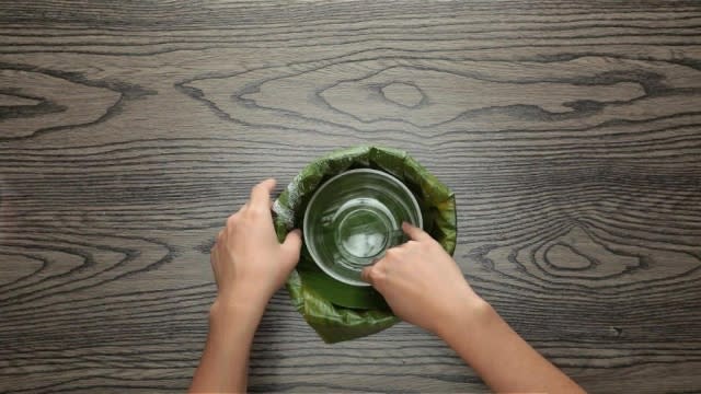 Pushing banana leaf into wrapped baking tin with a circular bowl