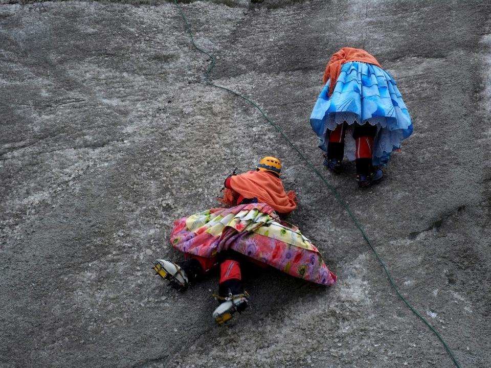 A photo of two women in bright skirts climbing up a sheer rock wall.