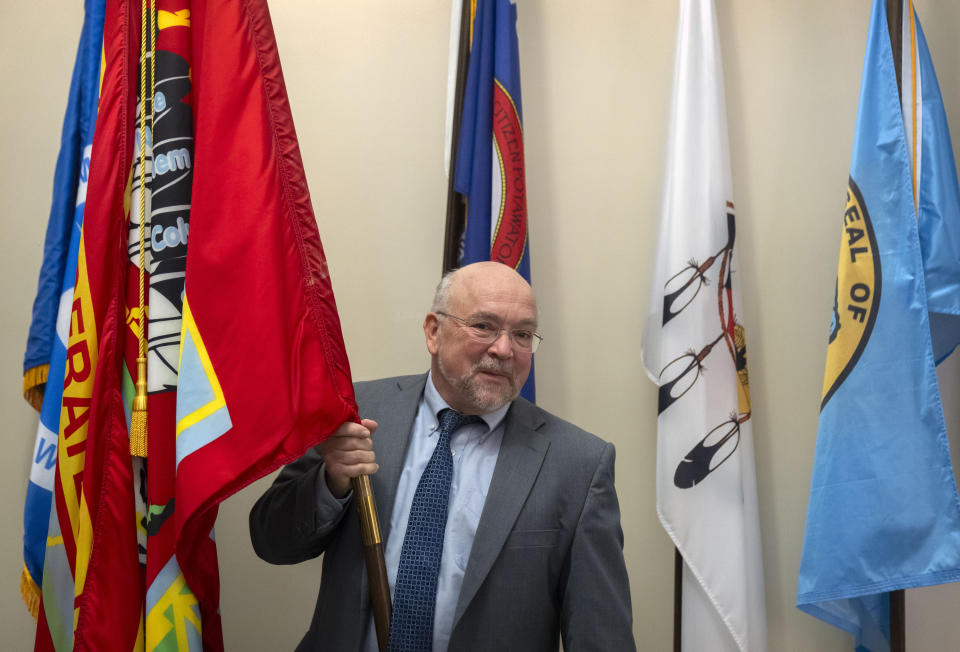 Tracy Toulou, the outgoing Director of the Office of Tribal Justice, holds the flag of the Colville Confederated Tribes, his tribal affiliation, alongside flags of tribal nations at the Department of Justice, Thursday, March 14, 2024, in Washington. For more than two decades, Toulou has confronted the serious public safety challenges facing Indian Country by working to expand the power of tribal justice systems. Today, tribal law enforcement finally has a seat at the table when federal authorities coordinate with state and local police, according to the Justice Department’s point person on Native American tribes. (AP Photo/Mark Schiefelbein)