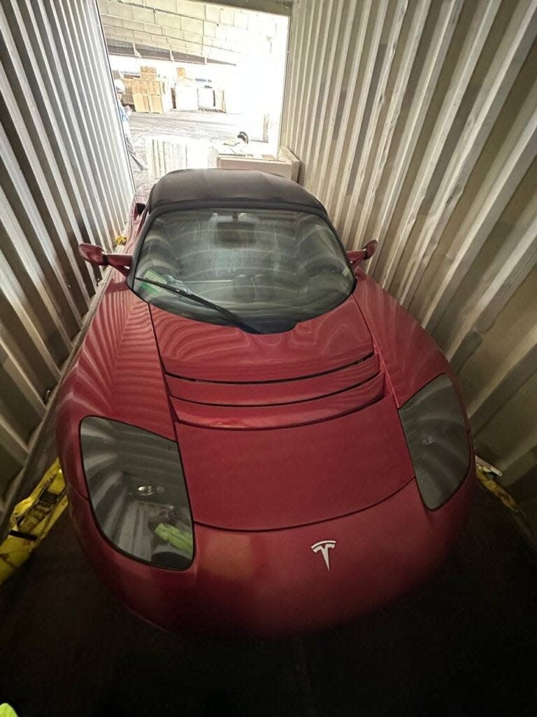 A red 2010 Tesla Roadster sits in a shipping container.