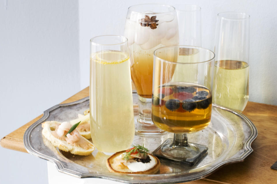 In this image taken on Jan. 28, 2013, from left clockwise, a glass of citrus bubbly with a small curl of lemon on top, a glass of spiced rose-pomegranate spritzer with a star anise on top, two glasses of sparkling wine, and a glass of wild meadow with berries, are shown with canapes and blini in Concord, N.H. (AP Photo/Matthew Mead)