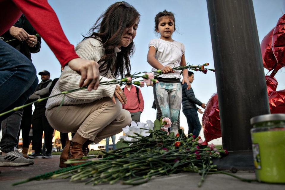 A woman and a girl place flowers at a memorial where community members gathered for a vigil.