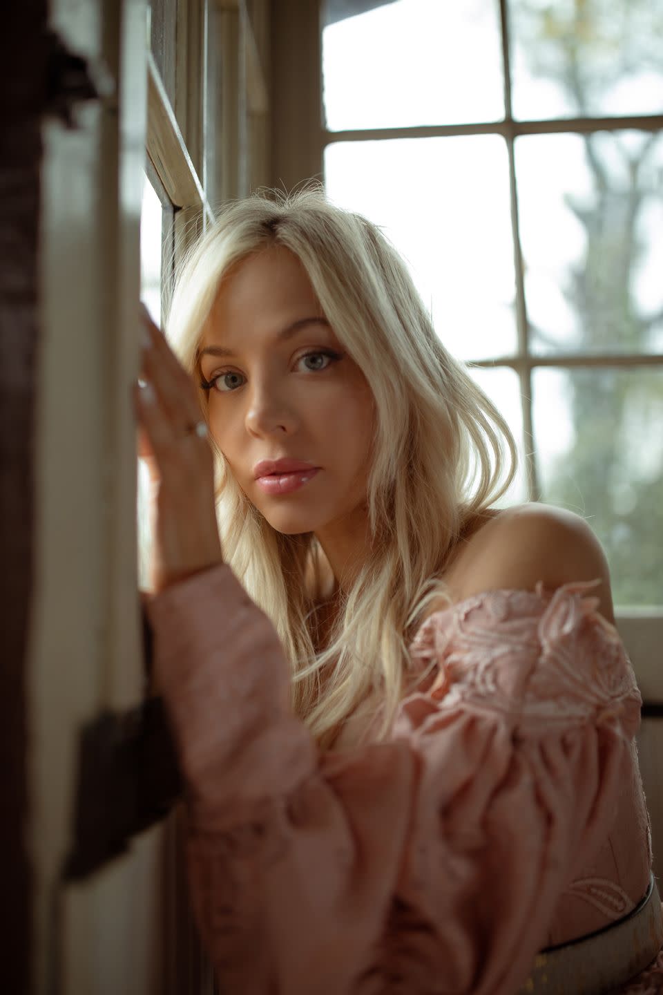 country singer songwriter mackenzie porter in pink off shoulder western style dress standing in farmhouse with natural light