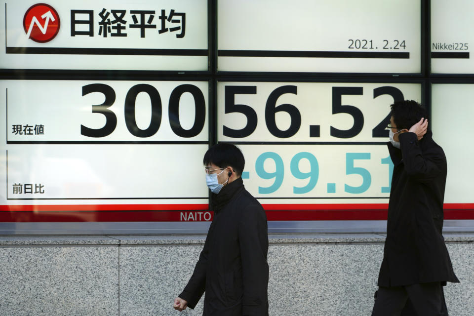 People wearing protective masks walk in front of an electronic stock board showing Japan's Nikkei 225 index at a securities firm Wednesday, Feb. 24, 2021, in Tokyo. Shares fell in Asia on Wednesday as investors weighed the possibility that inflation might prompt central banks to adjust their ultra-low interest rate policies. (AP Photo/Eugene Hoshiko)