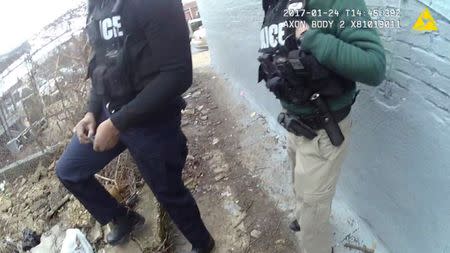 A still image captured from police body camera video appears to show two Baltimore police officers look on as a colleague places a small plastic bag in a trash-strewn yard (not shown) according to the Maryland Office of the Public Defender in this image released in Baltimore, Maryland, U.S. on July 19, 2017. Courtesy Baltimore Police Department/Handout via REUTERS