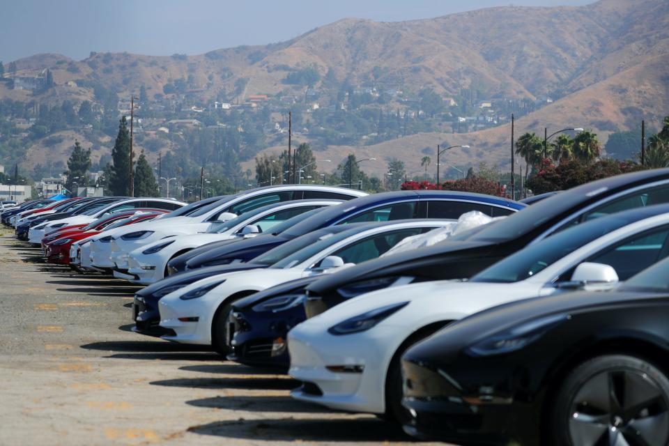 Newly manufactured Teslas sit in a lot in Burbank, California, against a mountainous backdrop.